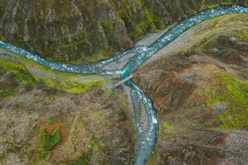 The aerial top down view of a milky blue river and a hiking trail path in Iceland.