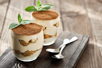 Classic dessert tiramisu in a glass on a wooden board on a sunny day.