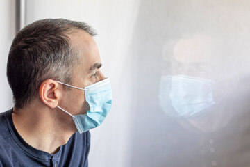 Young man with medical mask looking out the window