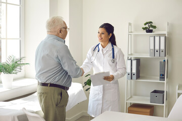 Fototapeta premium Friendly smiling woman physician meeting male elderly patient. Doctor and senior older man handshaking. Modern clinic office interior. Medicine, insurance and healthcare for retired people