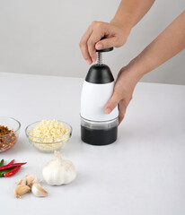 woman chopping garlic and chili with chopper tool on white table in the kitchen