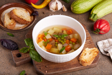 Broth with beef meat, green peas, zucchini, potato and carrot. Delicious homemade clear soup, served with basil leaves and toasts.