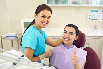 Happy client in dentist's office recommending dental clinic satisfied with good service provided by hygienist. Smiling female patient giving thumbs up and looking at camera during regular checkup