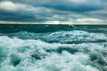 Heavy storm in the ocean. Big waves in the open sea, cloudy sky during a storm and a cargo ship on the horizon.