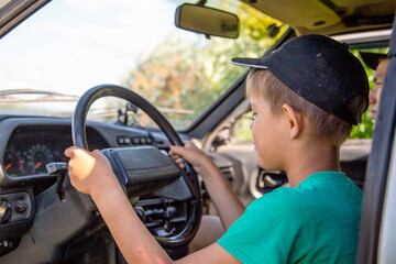 a boy in a cap sits at the wheel of a car