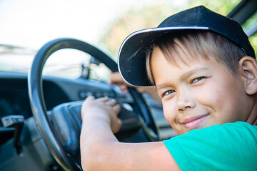 a boy in a cap sits at the wheel of a car