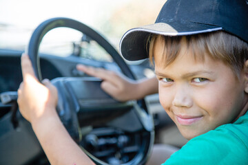 a boy in a cap sits at the wheel of a car