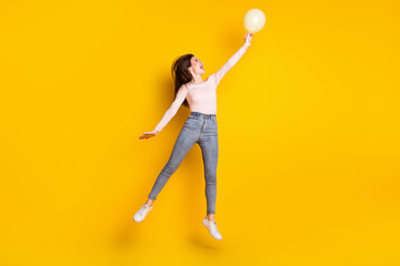 Full size profile side photo of young happy excited girl jumping look copyspace hold balloon isolated on yellow color background