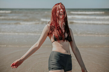 A young cheerful woman dancing in the waves by the sunny beach - obrazy, fototapety, plakaty