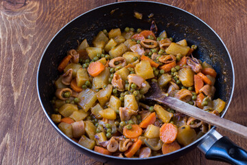 Squid with potatoes, peas and carrots cooked in a pan on wooden background