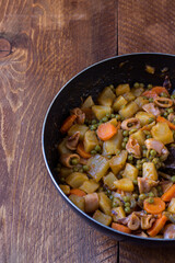 Squid with potatoes, peas and carrots cooked in a pan on wooden background