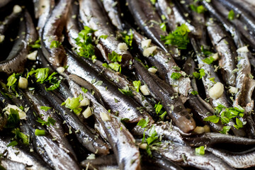 Close-up of fresh anchovies to be cooked in a pan with garlic and parsley.