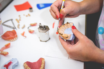 Close-up of a dental technician shaping a prosthesis tooth with a tool at work desk.