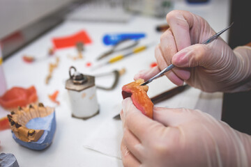 Close-up of a dental technician shaping a prosthesis tooth with a tool at work desk.