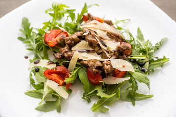 Cooked and cut meat with arugula, tomatoes annd parmesan flakes.