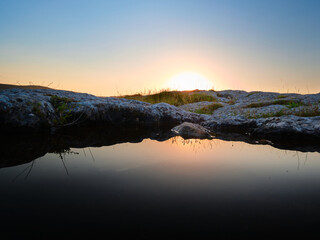 Rocks and vegetation reflecting in the water during the sunrise in the mountain