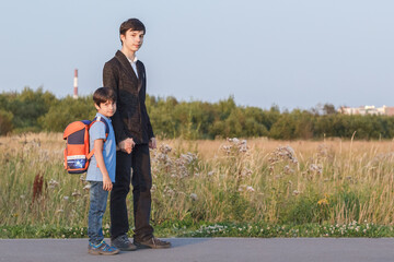Brothers go to school. The teenager and his younger brother with backpacks hold hands, brothers smile happy faces of children. back to school