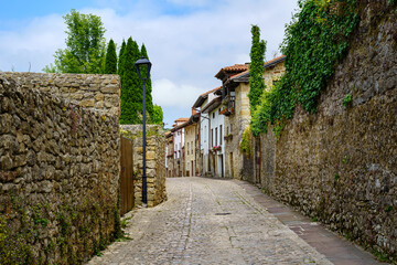 Old stone village street with walls covered with greenery and flowers. Santillana del Mar.