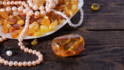Transparent  yellow and orange Baltic amber stones and iridescent pink pearls close up on a dark...