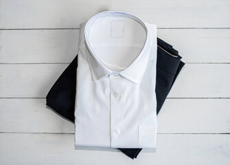 White shirt and black dress slacks pants folding on white wooden background.