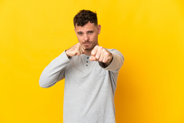 Young caucasian handsome man isolated on yellow background with fighting gesture