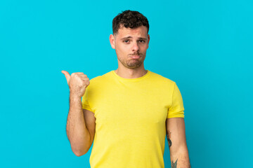Young caucasian handsome man isolated on blue background unhappy and pointing to the side
