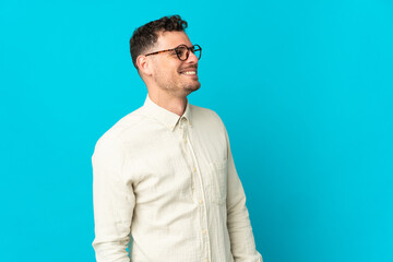 Young caucasian handsome man isolated on blue background looking to the side and smiling