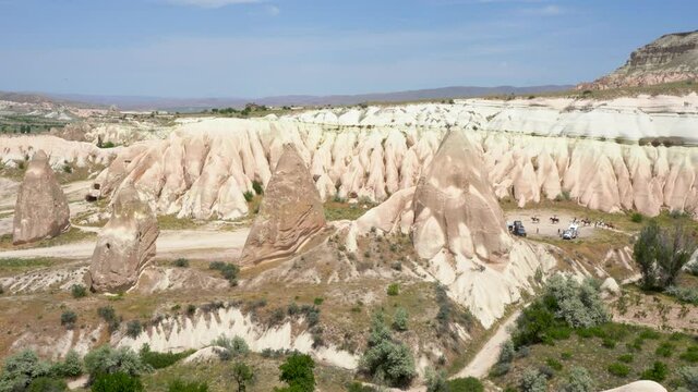 4k stock video footage of scenic landscape of rocky Cappadocia. Mountains, blue sky, people riding on horses, trailers parked on camping site. Tourism in Turkey concept
