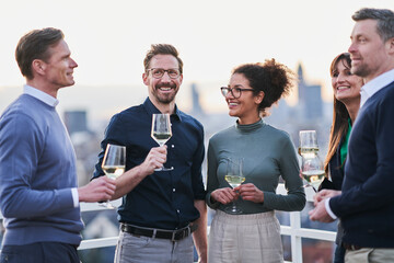 Smiling male and female entrepreneurs standing with wineglasses on building terrace