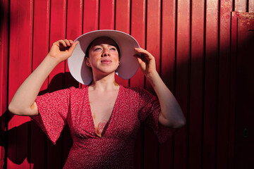 Young woman looking away wearing sun hat by red wall