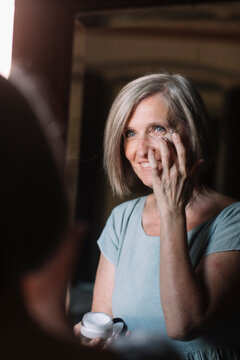 Smiling woman looking in mirror while applying cream at home