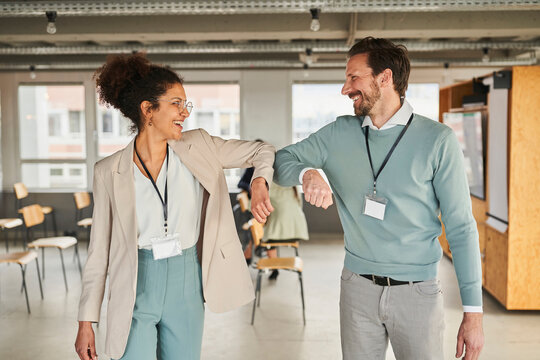 Smiling male and female colleagues greeting with elbow bumps in conference centre