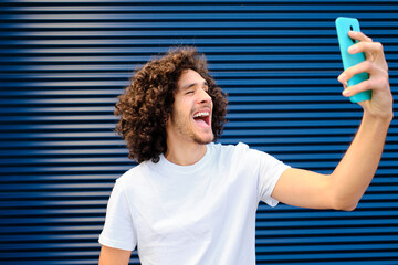 Cheerful young man making face while taking selfie through mobile phone