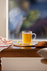 Green herbal tea in a clear glass cup with fresh french pastry, decorated with yellow flowers, served on small wooden table on the terrace or balcony