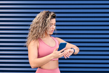 Young athlete with mobile phone checking time on wristwatch by blue wall
