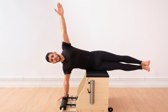 Determined man lying sideways with arm raised on pilates chair in exercise room