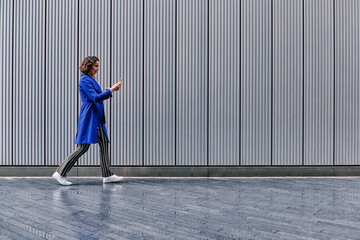 Female professional using smart phone while walking on footpath