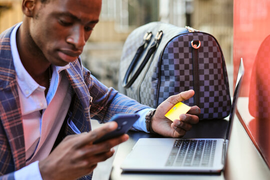 Businessman With Credit Card Using Mobile Phone At Sidewalk Cafe