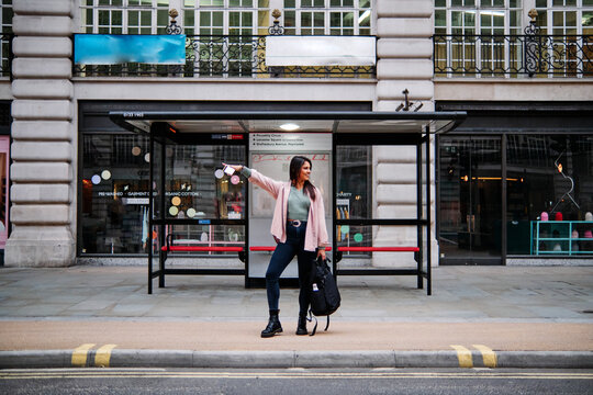 Smiling woman hailing while waiting at bus stop in city