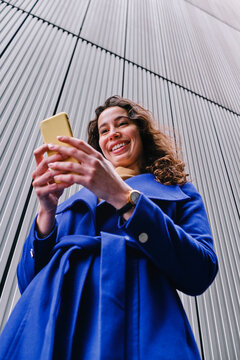 Smiling female professional working on smart phone in front of wall