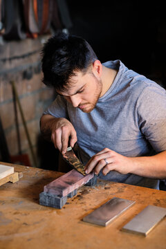 Male metal worker sharpening knife on table at workshop