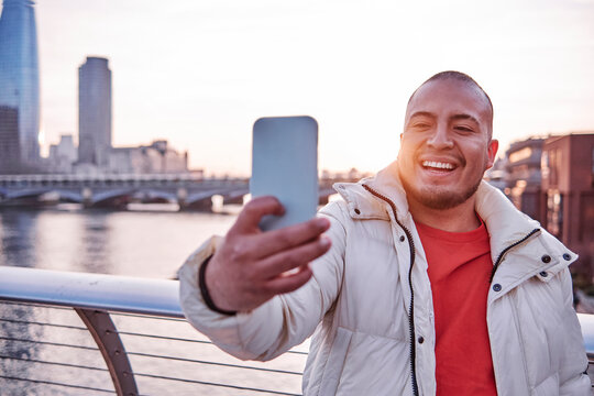 Smiling young man taking selfie from smart phone by railing during sunny day