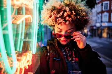 Woman wearing sunglasses by illuminated neon lights
