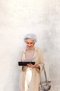 Woman with shopping bay using digital tablet in front of wall