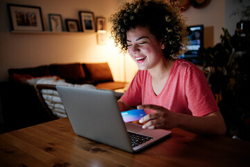 Cheerful young woman with laptop doing online shopping at home