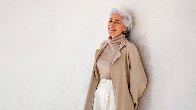 Smiling woman in trench coat leaning on wall