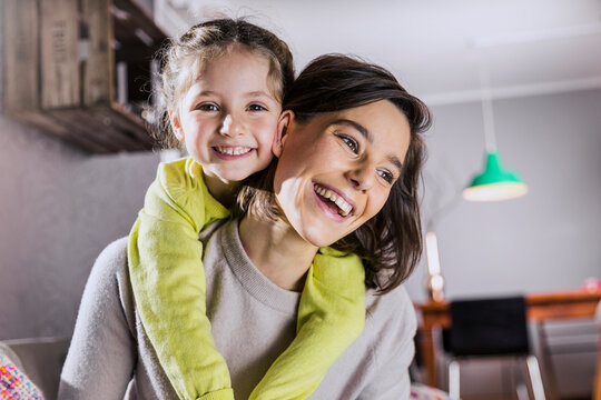 Smiling mother piggybacking daughter at home