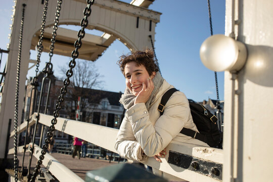 Smiling young woman leaning on railing at bridge