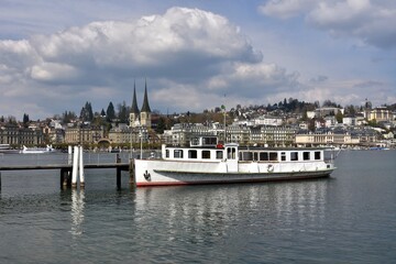 Fototapeta na wymiar Tourist motor vessel moored in the harbor of city of Lucerne situated on Lake Lucerne during sunny day with heap cloud, On the background is visible historic city of Lucerne.