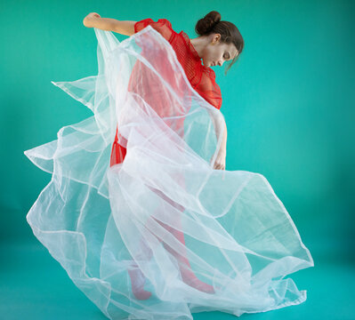 Young ballerina dancing with white tulle against turquoise background